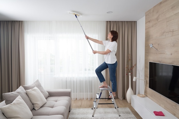 woman cleaning ceiling with a mop. housewife cleaning living room