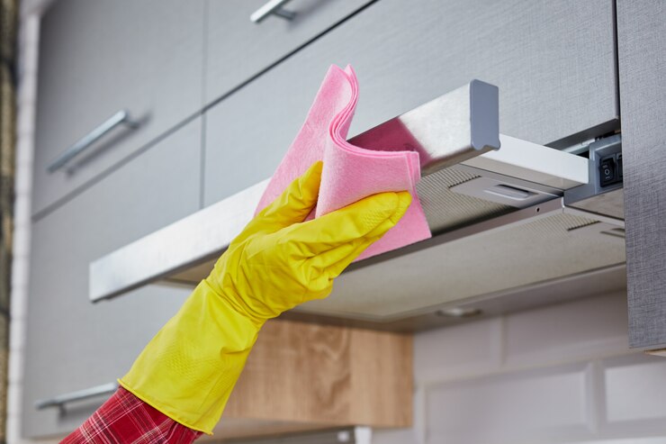 Photo woman cleaning cooker hood with rag in kitchen. close up of female hand in rubber protective yellow gloves clean the kitchen metal extractor hood with rag. home, housekeeping concept