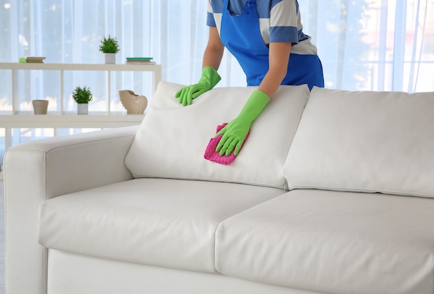 Woman cleaning couch with duster at home