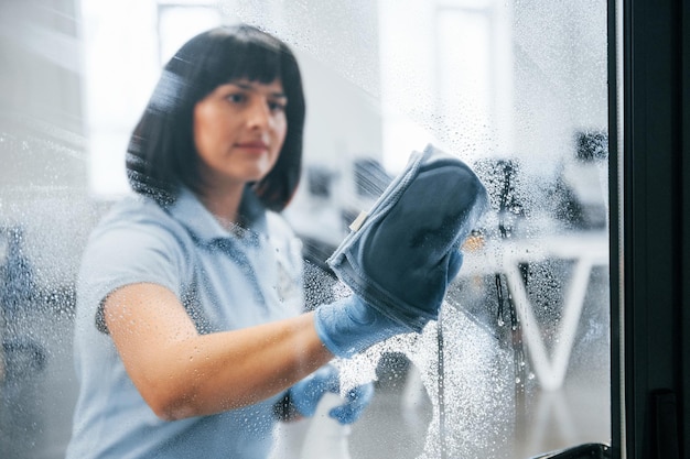 Woman cleaning dirty window by using towel View through the glass