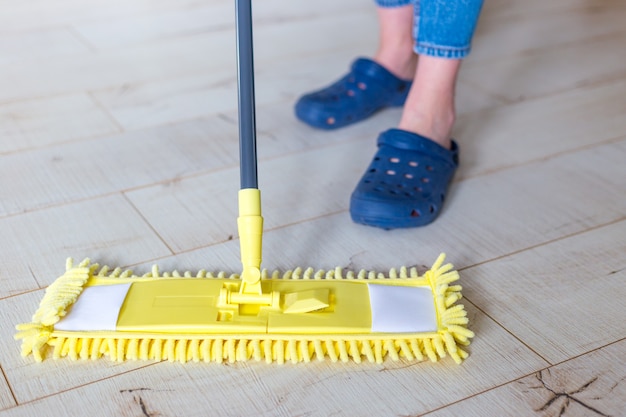 Woman cleaning floor with yellow mop at home. microfiber mop
isolated on white wooden floor background, closeup, indoors