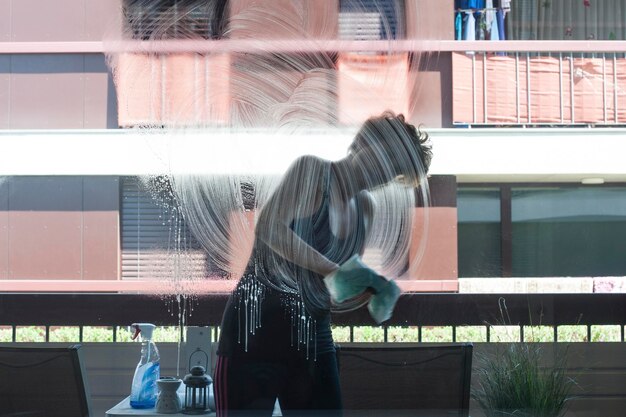 Foto donna che pulisce la parete di vetro a casa