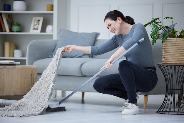 Woman cleaning home and with broom sweeping carpet for daily chores cleanliness and doing housework Cleaner domestic and lady complete duties clean under mat for dust health and hygiene