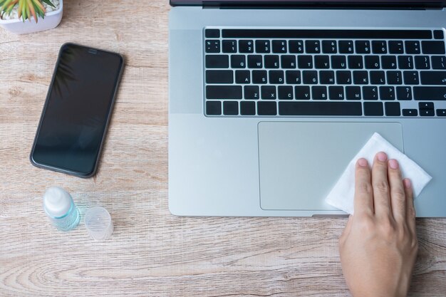 Woman cleaning laptop with wet wipe and disinfectant