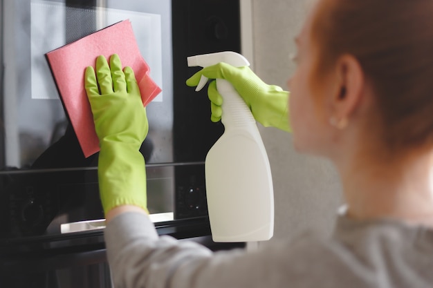 Woman cleaning oven and microwave with rag in kitchen, close up