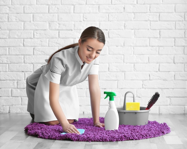 Woman cleaning small rug near white wall