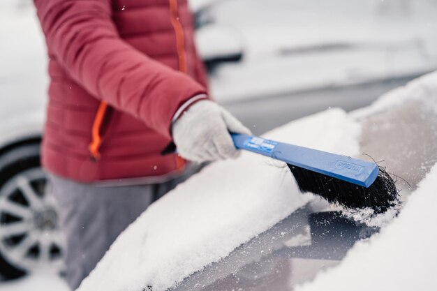 冬の降雪時に車の雪を掃除する女性 氷をかき出す 冬の窓掃除