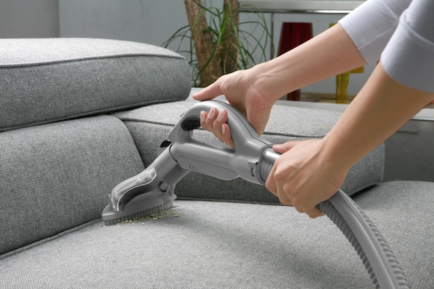 Woman cleaning sofa with vacuum cleaner