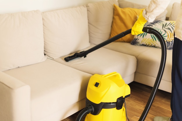 Woman cleaning sofa with yellow vacuum cleaner. clean concept