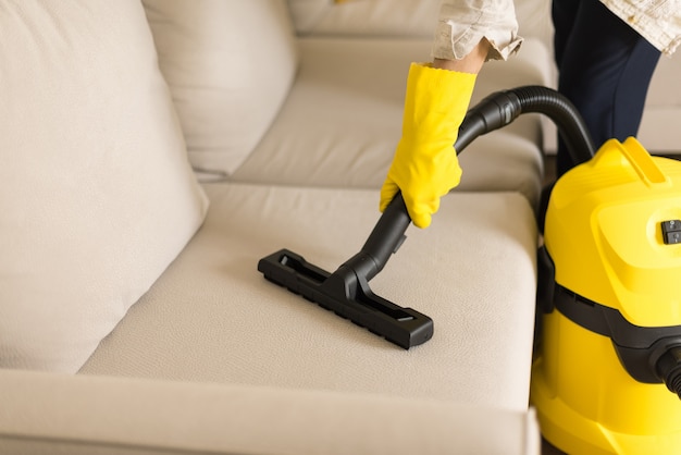 Photo woman cleaning sofa with yellow vacuum cleaner. copy space. clean concept