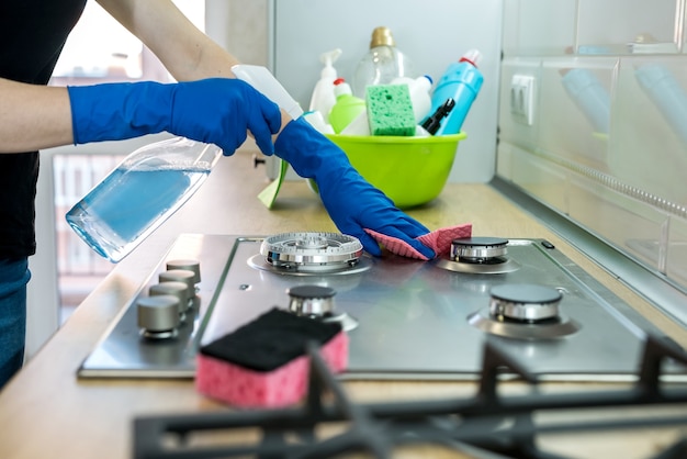 Woman cleaning stainless steel gas surface in the kitchen with rubber gloves.