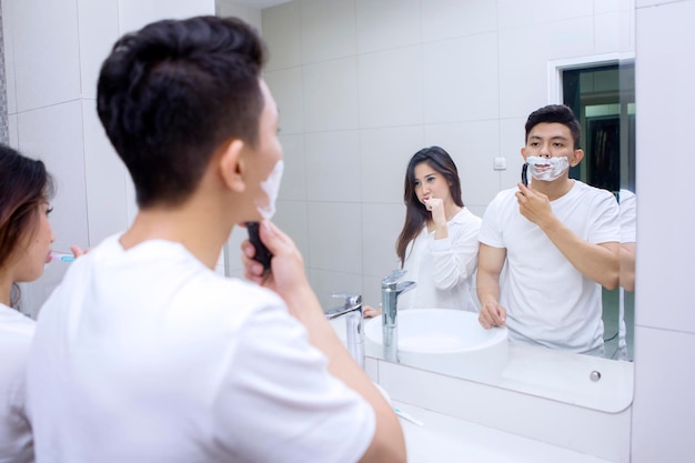 Woman cleaning teeth and her husband shaving his beard