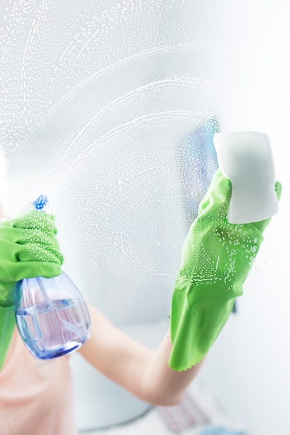 Woman cleaning window pane with detergent, cleaning concept.