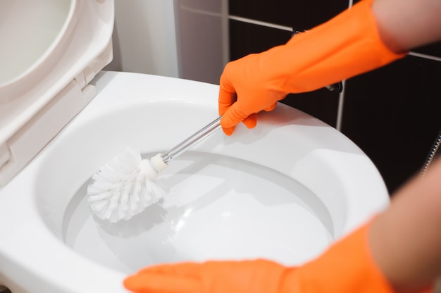 A woman cleans a bathroom toilet with a scrub brush.