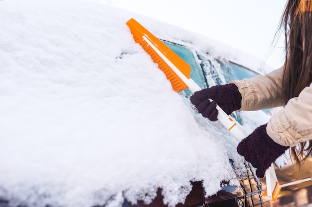 Woman cleans car with brush from snow