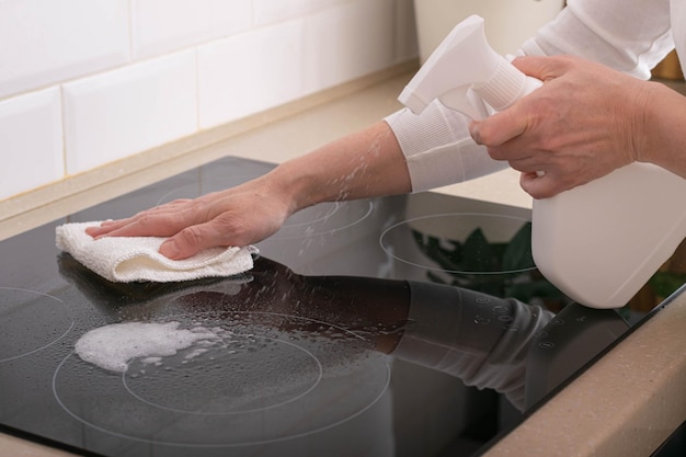 여자는 주부들의 집안일에 세제로 세라믹 난로를 청소한다.