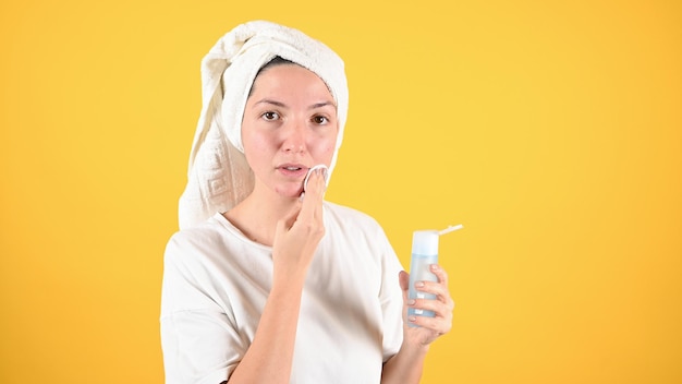 Woman cleans her face with cotton pads removing makeup on yellow background Daily morning routine