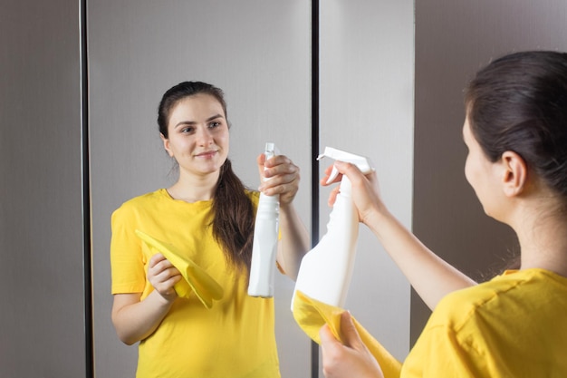 A woman cleans the mirror with a water dispenser and window cleaner.