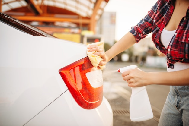 Woman cleans rear lights of the car with spray