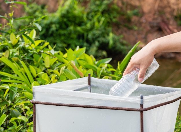 Woman cleans up by picking up plastic bottles at a natural water reservoir Concept of protecting environment saving world recycling reducing global warming Earth Day close up blurred background