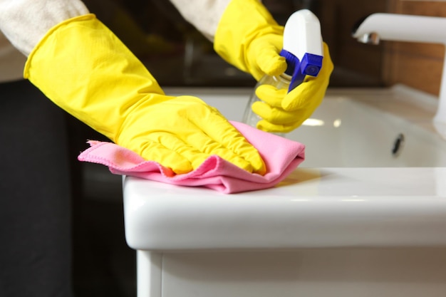 Женщина моет раковину и кран в уборке и дезинфекции ванной комнаты