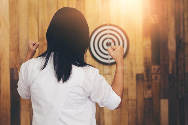 Photo woman clenching fists while standing against dartboard