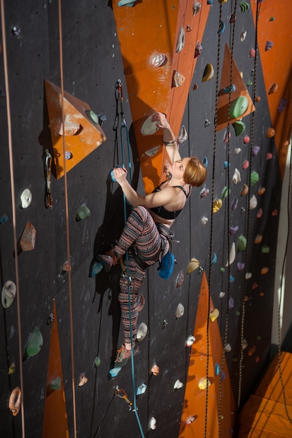 Woman climber is climbing up on indoor climbing wall and looking up