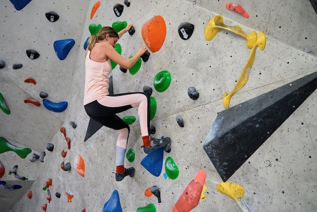 Woman climbing up on wall at bouldering gym, female climber training