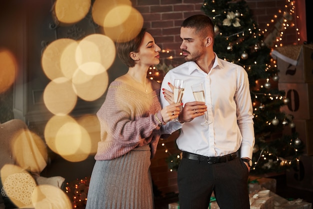 Woman clings to her husband. Nice couple celebrating new year in front of Christmas tree