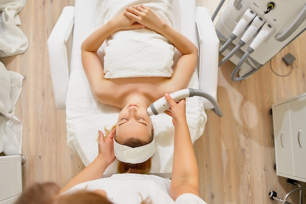 Woman close up receiving electric facial massage on microdermabrasion equipment at beauty salon.