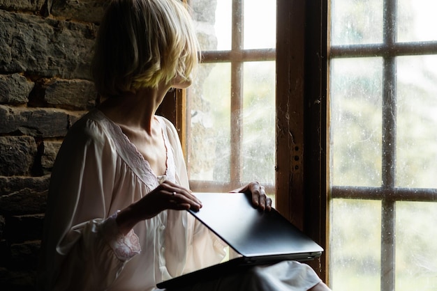 Женщина закрывает ноутбук у окна Конец работы Фрилансер работает из дома
