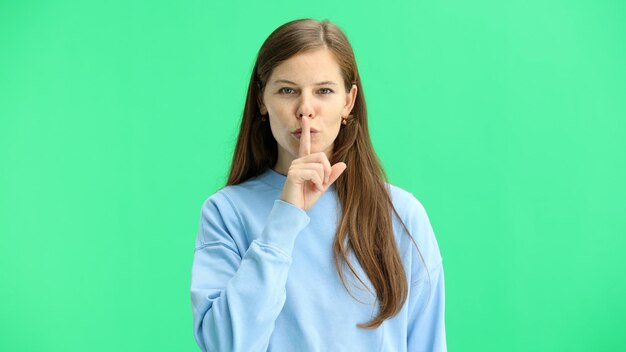 Foto una donna in primo piano su uno sfondo verde mostra un segno di silenzio