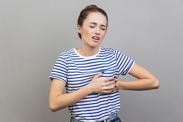 Woman clutching breast and grimacing from painful cramp heart\
attack at young age cardiac disease