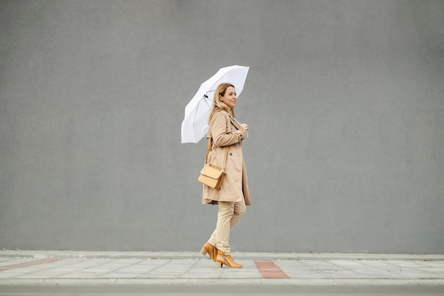 A woman in a coat is walking on the street with umbrella in her hands on a rainy autumn day