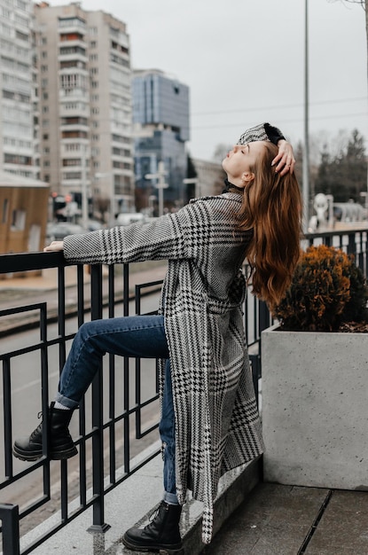 A woman in a coat and jeans leans on a railing