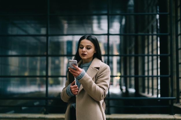 Woman in coat using smartphone on street