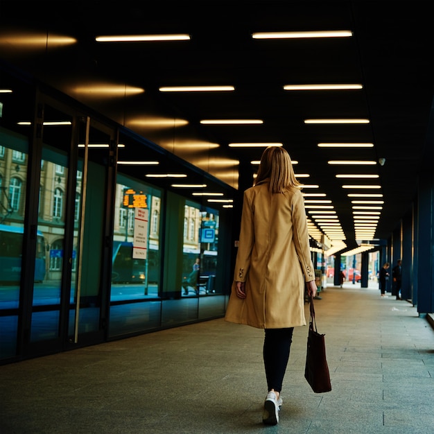 La donna in cappotto cammina per la strada della città con la borsa