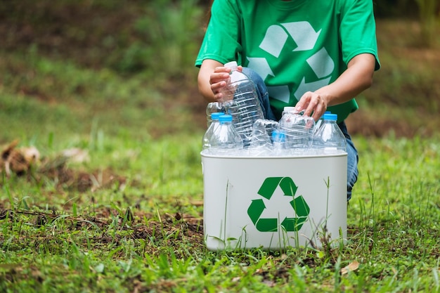 a woman collecting and putting plastic bottles into a recycle bin in the outdoors