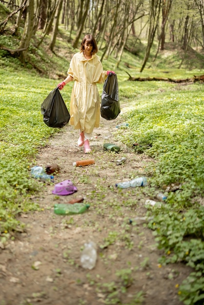 Woman collecting scattered plastic garbage in the woods