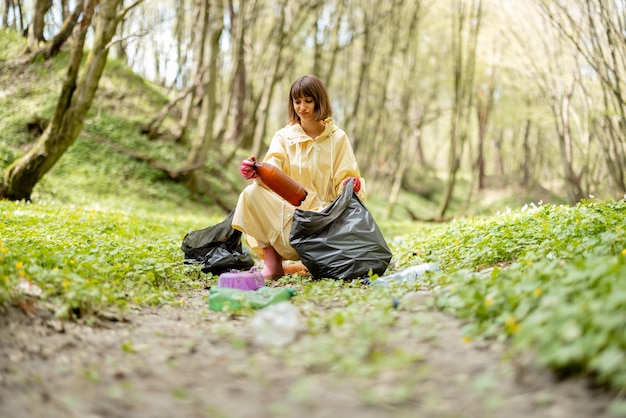 Woman collecting scattered plastic garbage in the woods