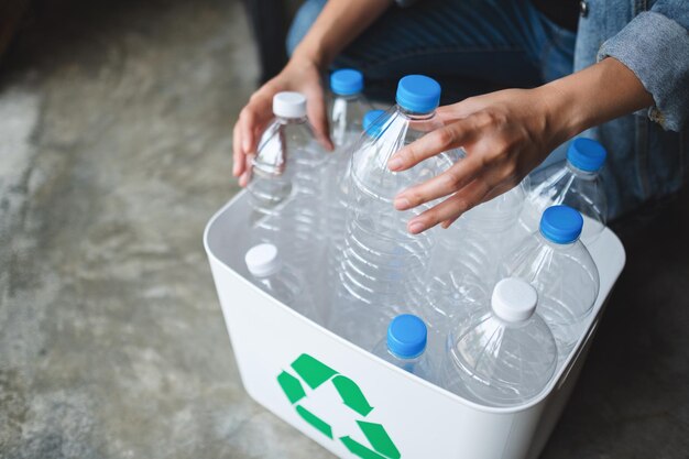 A woman collecting and separating recyclable garbage plastic bottles into a trash bin at home