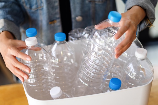 A woman collecting and separating recyclable garbage plastic bottles into a trash bin at home