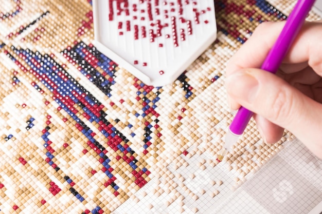 A woman collects a diamond mosaicthe process of creating a\
picture of multicolored rhinestones diamond mosaic painting\
fragment of making closeup top view handmade hobby