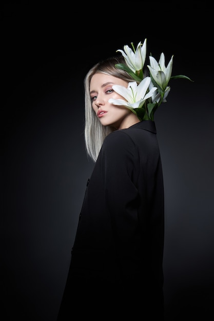 Woman colored hair color of a blonde with lily flower on black background.