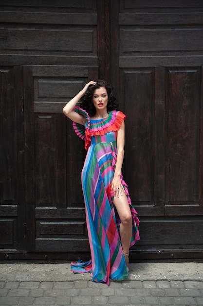 A woman in a colorful dress stands in front of a door.