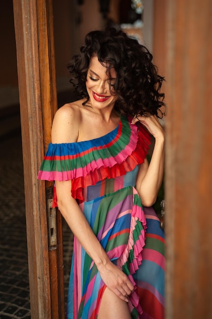 A woman in a colorful striped dress stands in a doorway and smiles.