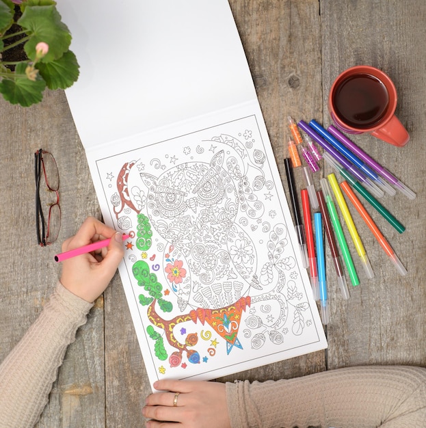 Woman coloring an adult coloring book and drinking tea new stress relieving trend mindfulness concept married woman top view