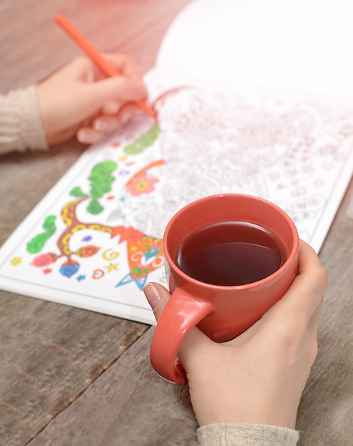 Woman coloring an adult coloring book and drinking tea new stress relieving trend mindfulness concept married woman