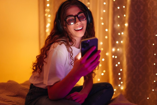 Foto la donna comunica con gli amici sullo smartphone in cuffia mentre è seduta a casa concetto di freelance