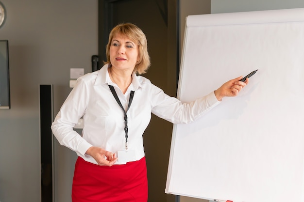 A woman conducts training in a business center. Middle-aged woman coaching at the flipchart Board in business style.